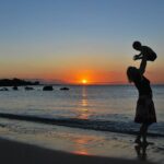 夕暮れの海岸で子供を高く抱き上げる女性