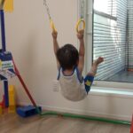 鉄棒に付けられた吊り輪に掴まってぶら下がる1歳児