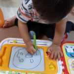 お絵描きボードにアンパンマンの顔を描く2歳児